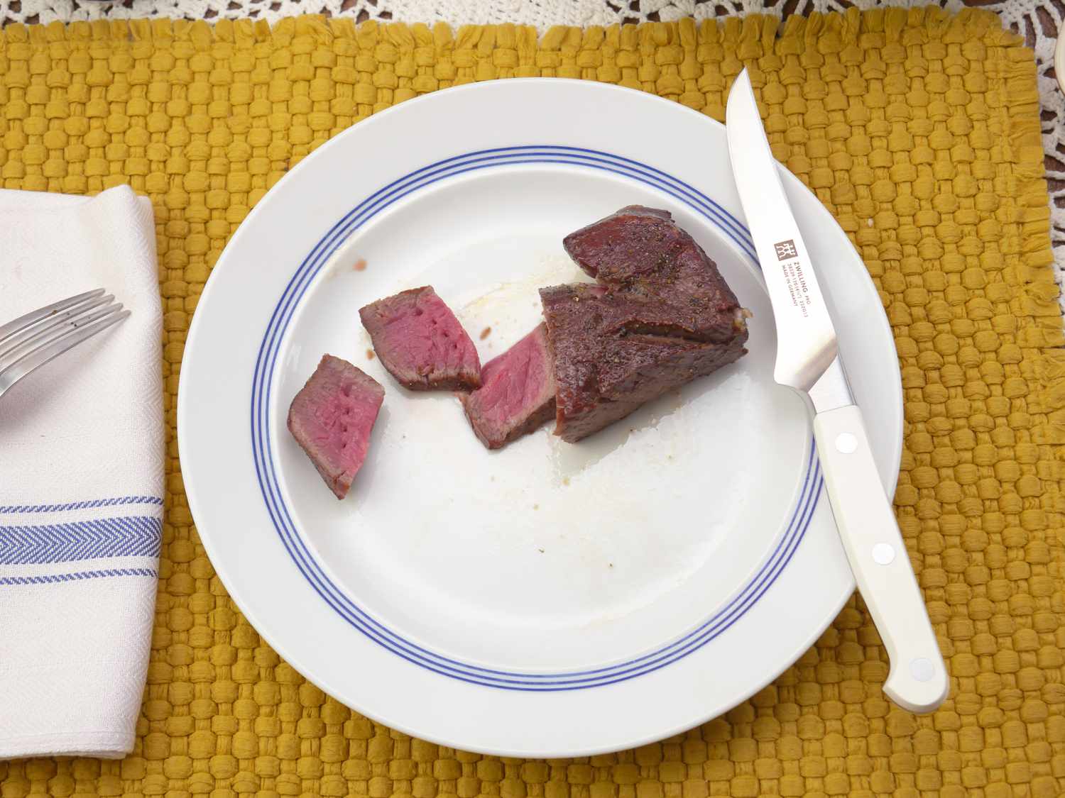 the zwilling le blanc steak knife resting on a white plate with sliced meat
