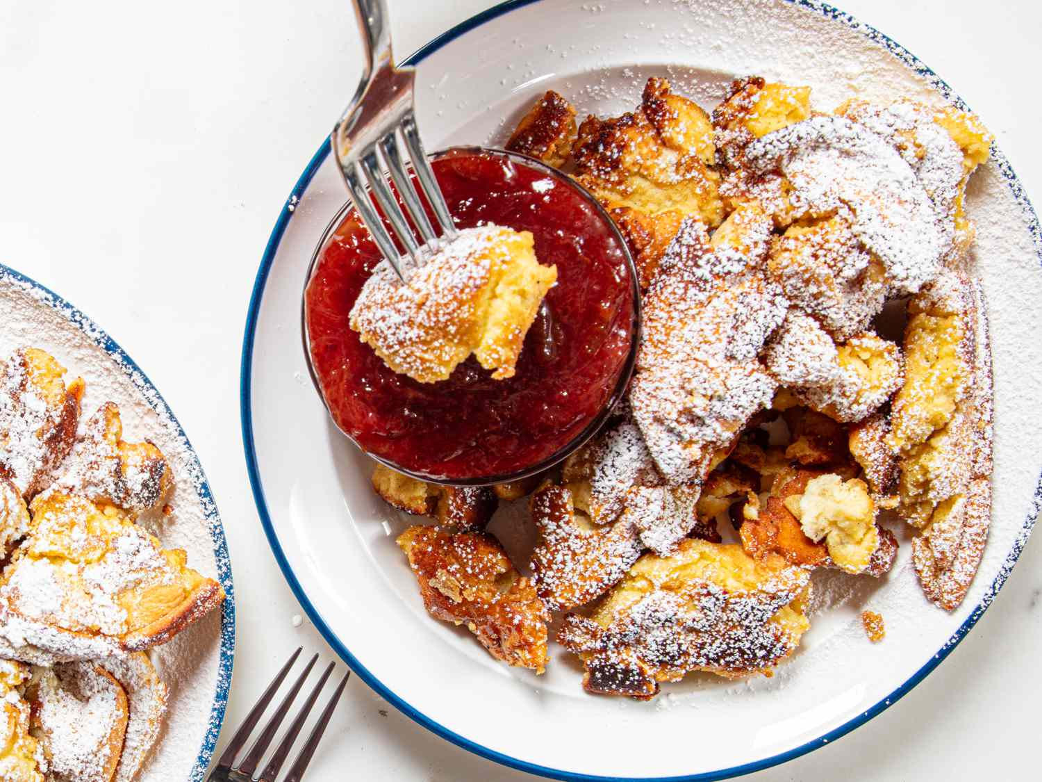 Kaiserschmarrn served with a side of red fruit jam on a plate with a fork lifting a piece of the dish