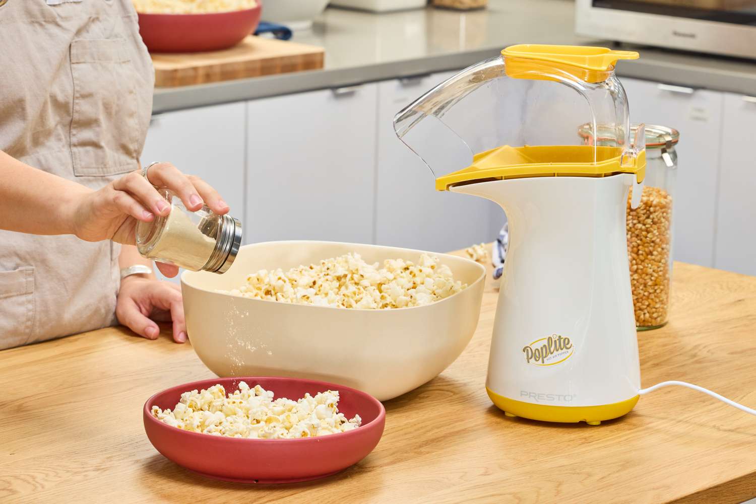 A person sprinkles seasoning onto the Presto Poplite Hot Air Popper