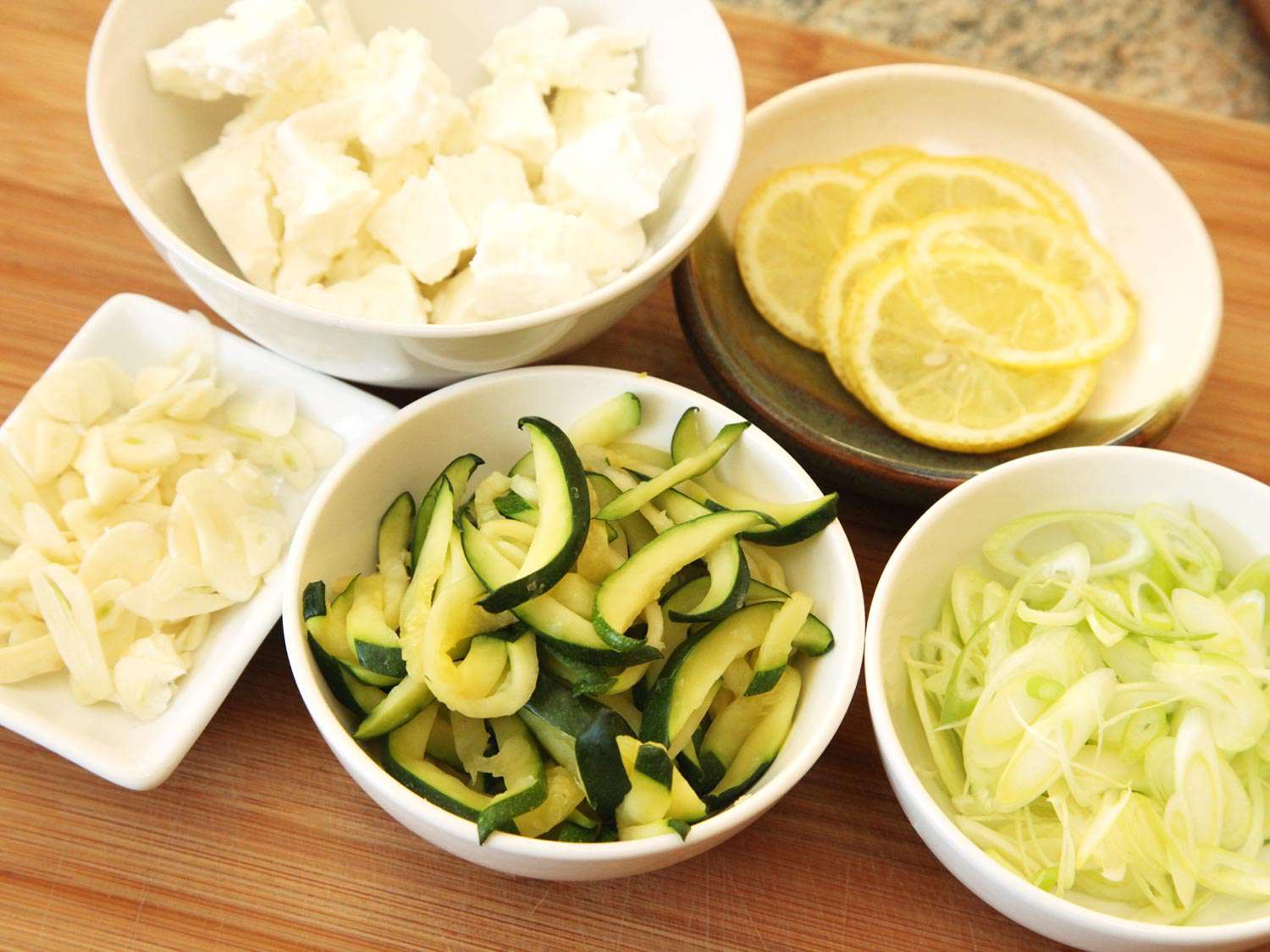 Toppings for zucchini pizza assembled in several bowls.