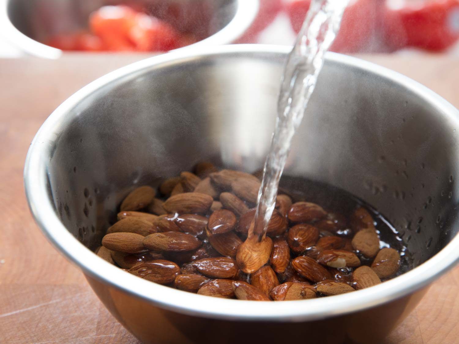 Boiling water is poured over almonds in a metal bowl.