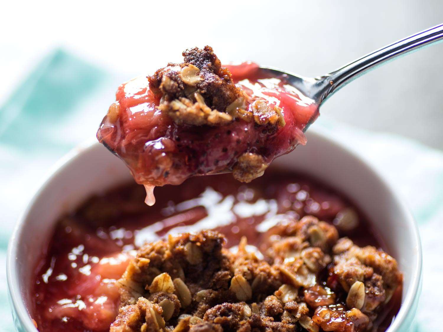 A spoonful of strawberry-rhubarb crisp being lifted from a white bowl