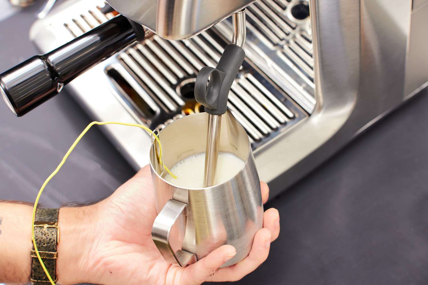 A person steaming milk in a pitcher with a Breville espresso machine.