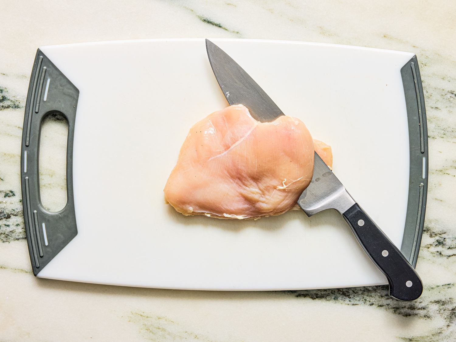A chicken breast with a knife on a cutting board