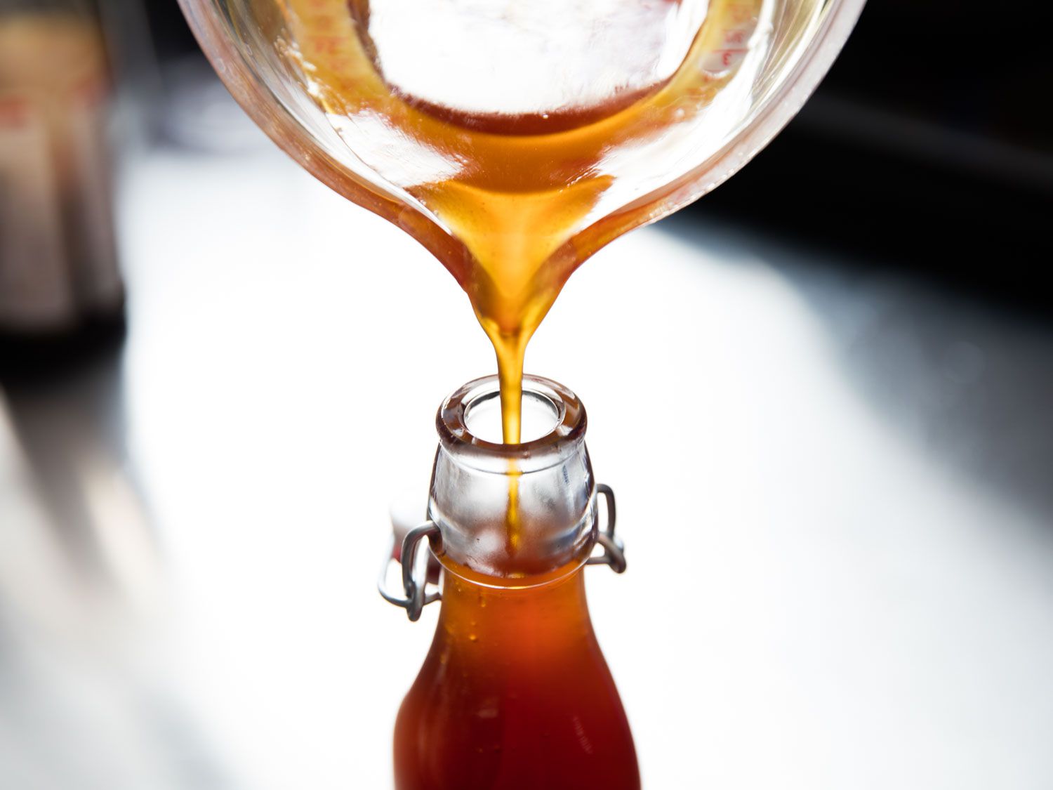 Pouring golden-brown syrup into a flip top glass bottle.