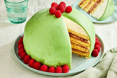 A sliced Princess cake garnished with raspberries on a plate showing its layered interior filling and marzipan cover