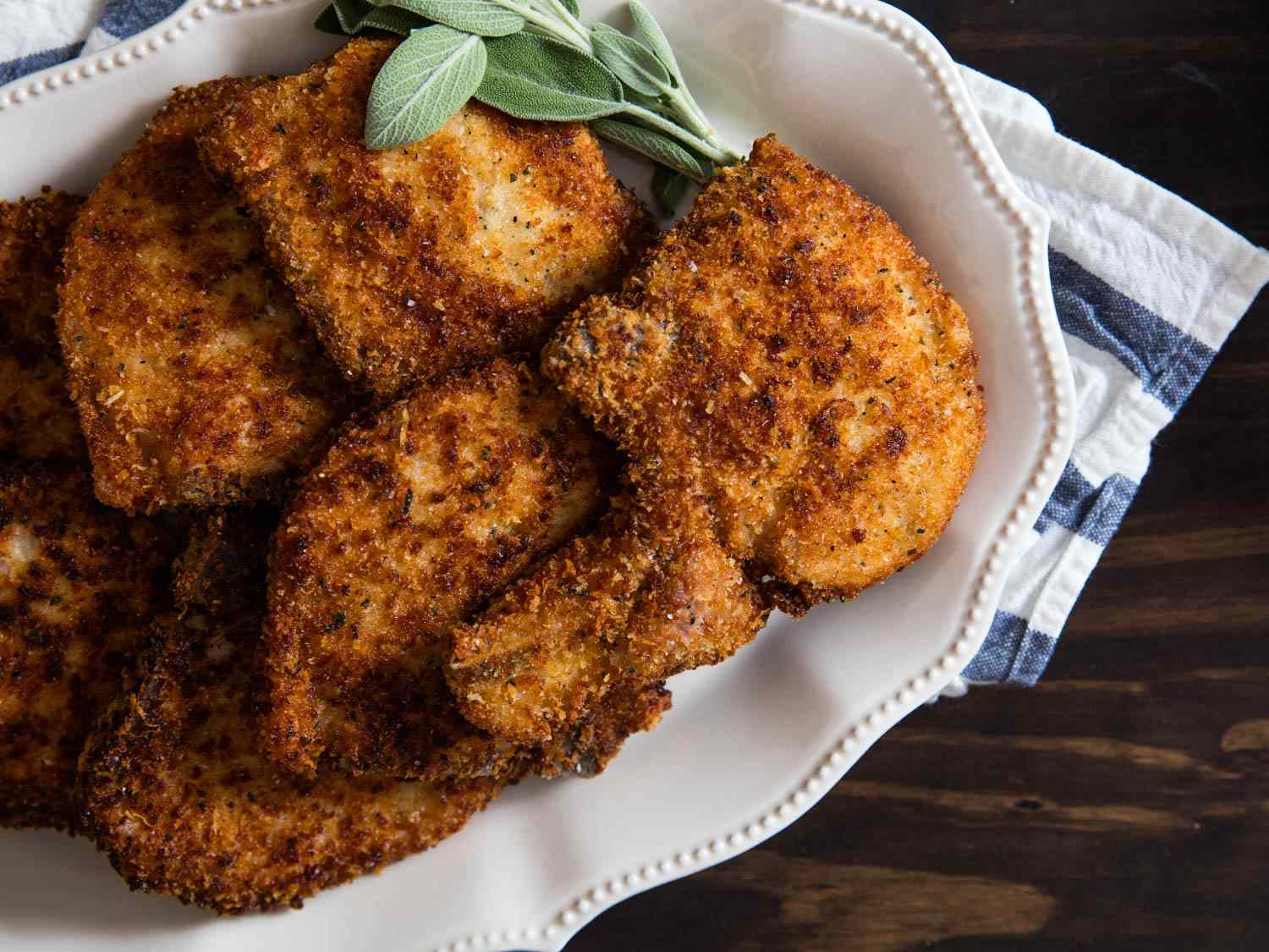 A platter of golden-brown fried pork chops garnished with fresh sage.