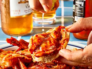 A hand squeezing lime onto a shrimp dish with sauce on a plate beer bottles in the background