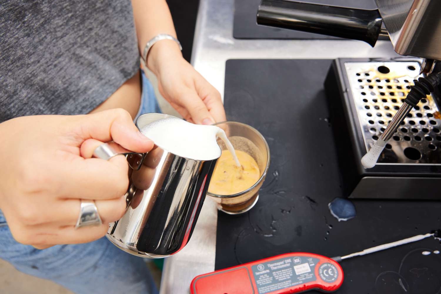 A person pouring in milk into the espresso in a glass 