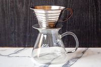 A metal coffee dripper sitting on a glass carafe