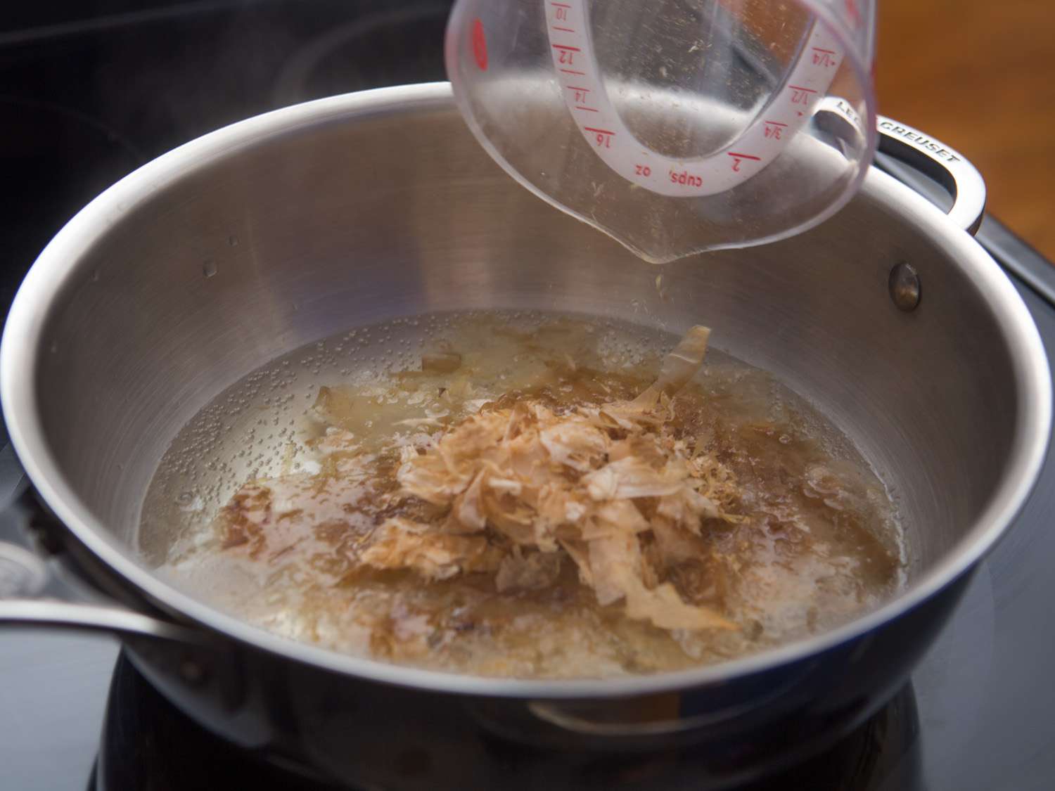 Adding bonito flakes to a pan of kombu broth.