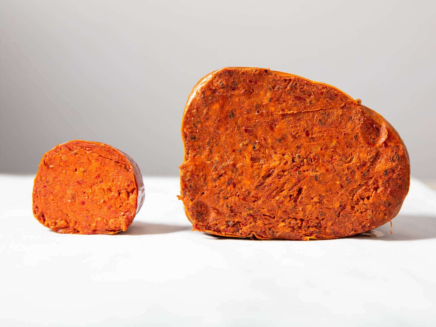 Two cuts of 'nduja with a small one on the left and a large on the right.