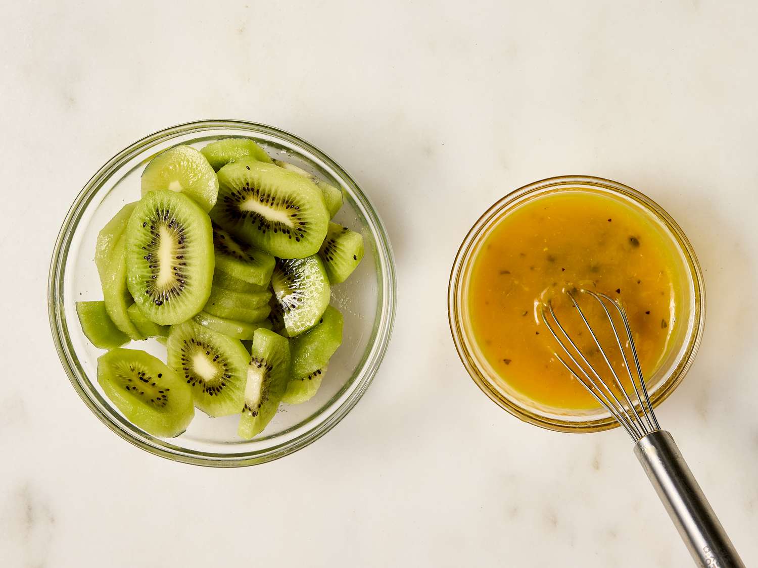 Sliced kiwis in a bowl next to a whisk in a bowl of passionfruit sauce
