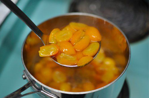 Ladling simmered kumquat halves in syrup.