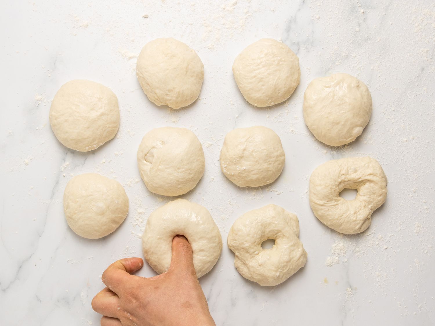 Shaping dough pieces into doughnuts on a countertop