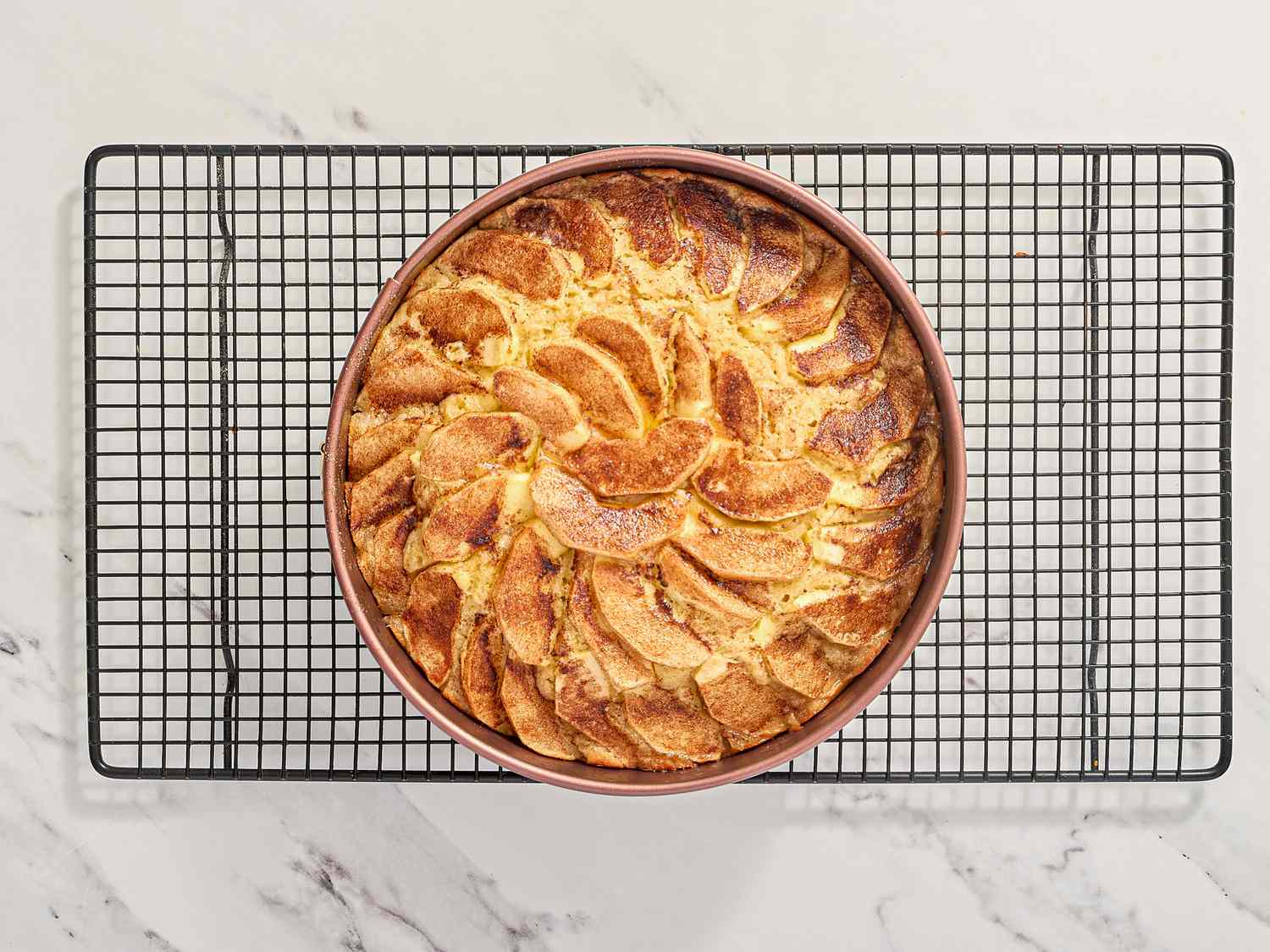 A baked apple cinnamon cake on a cooling rack on a marble surface