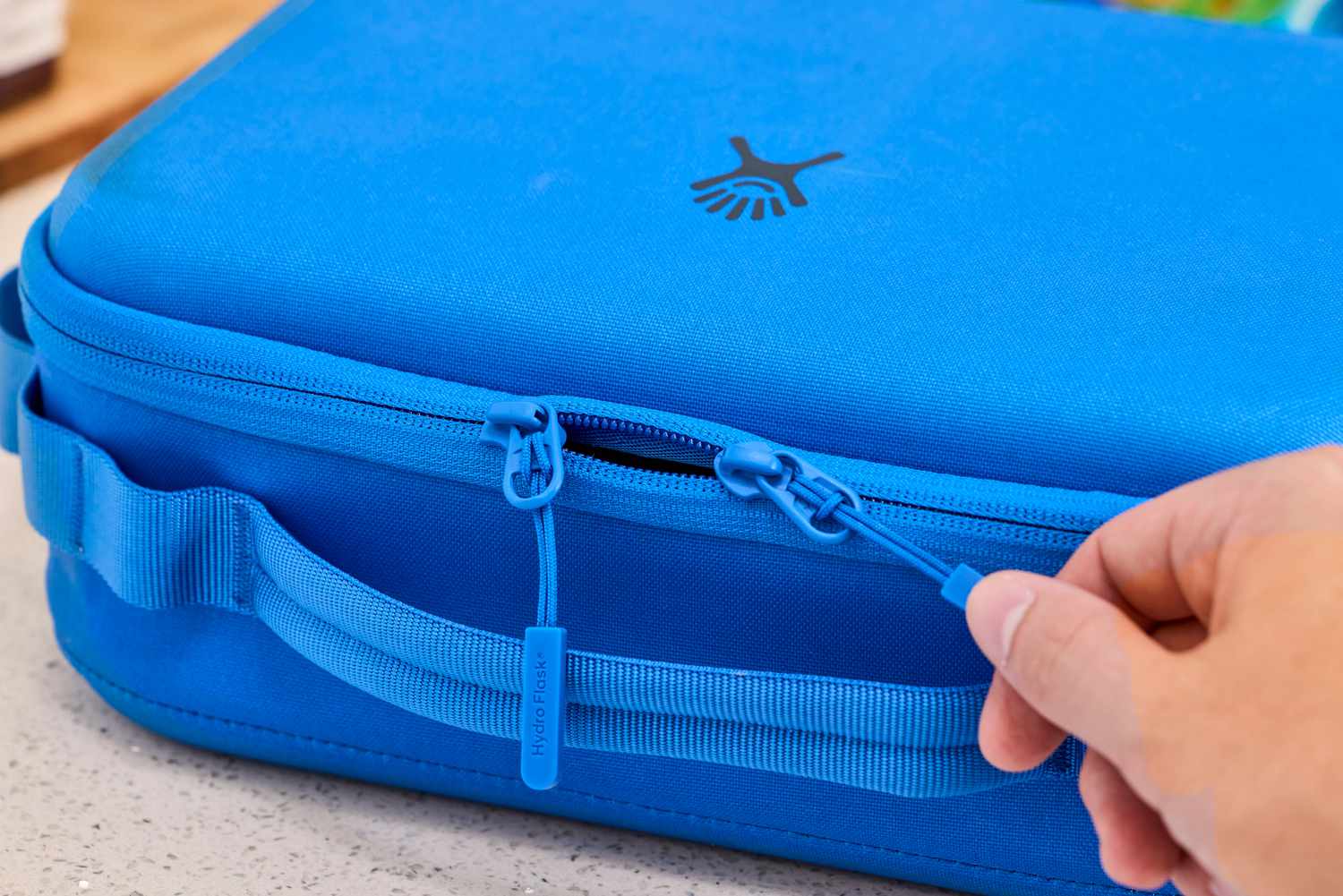 A zipper being pulled open on a blue lunch box.