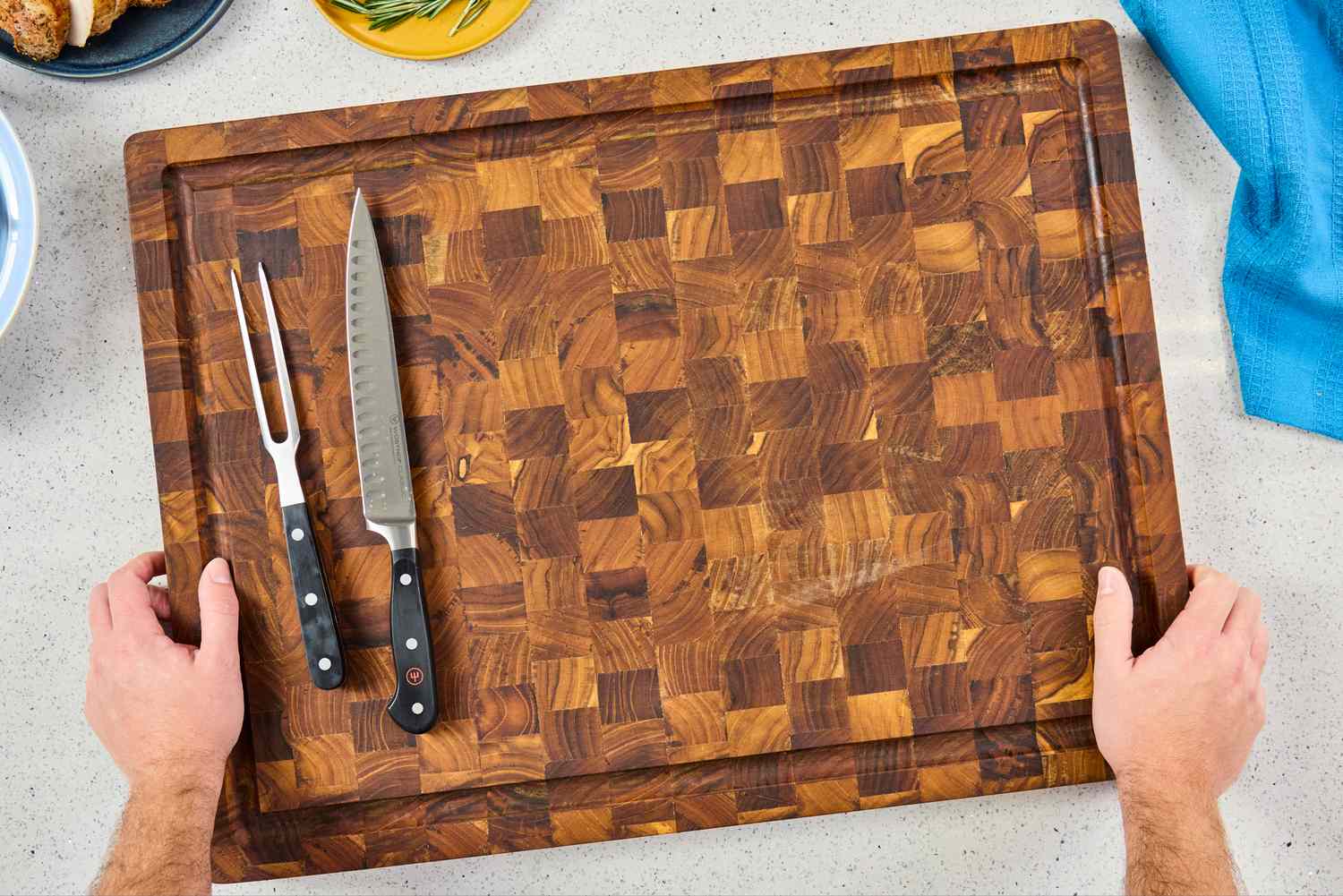 An overhead view of a Yes4All Teak Cutting Board with a meat fork and slicing knife on the lefthand side