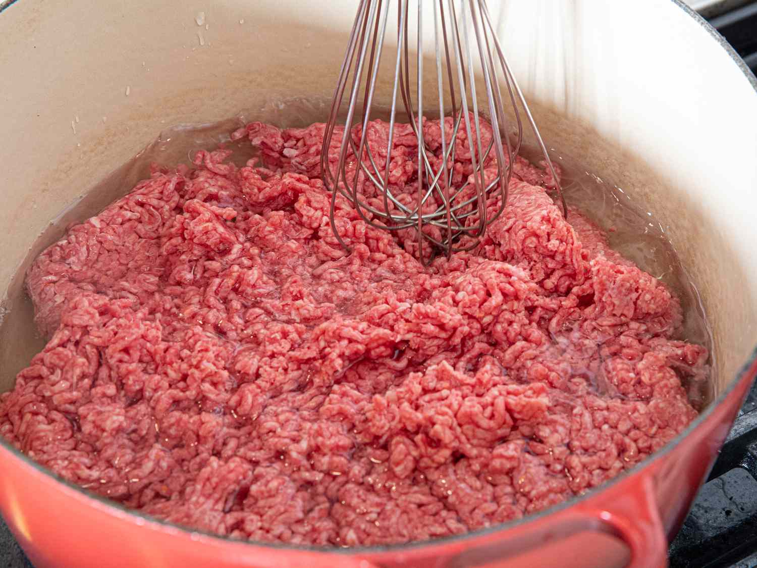 Side view of mashing beef with whisk
