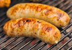 Two links of roasted garlic and feta chicken sausage, browning on the grill.