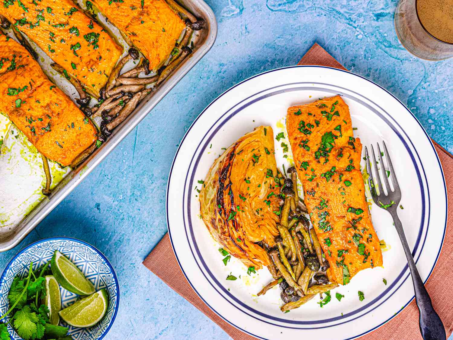 A plated salmon dish alongside a sheet pan with prepared salmon and vegetables, garnished and ready to serve