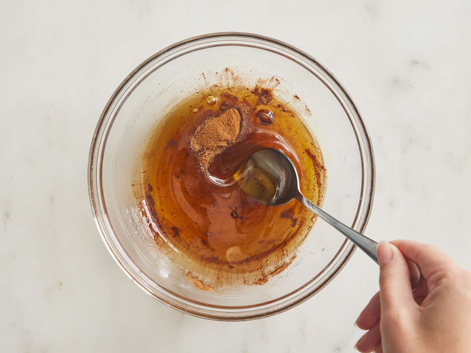 Stirring nutmeg and cinnamon into melted butter in a glass bowl.