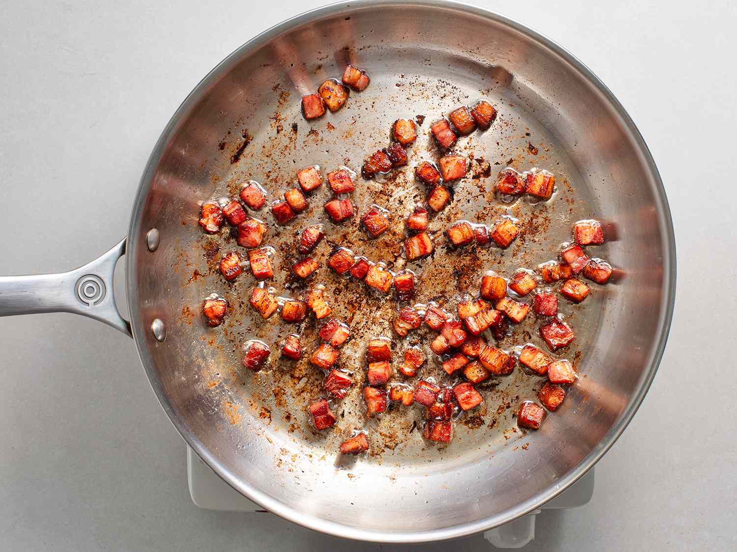 Bacon being fried in a stainless steel skillet.