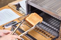 A person using tongs to take toast from a breville compact toaster oven