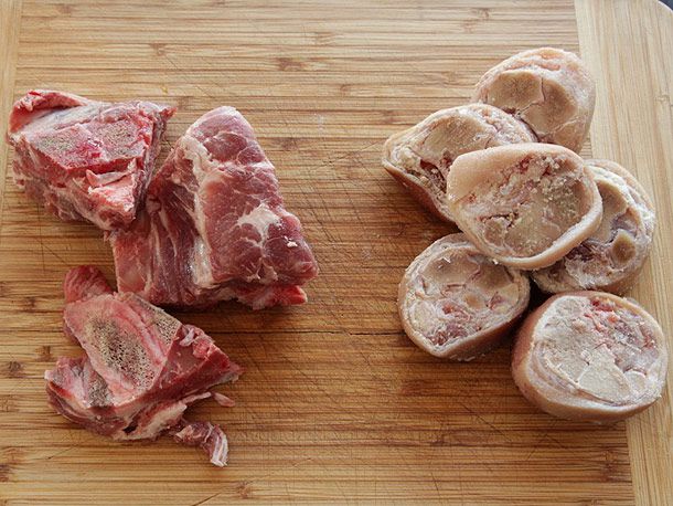 Pork trotters and pork neck bones on a cutting board.