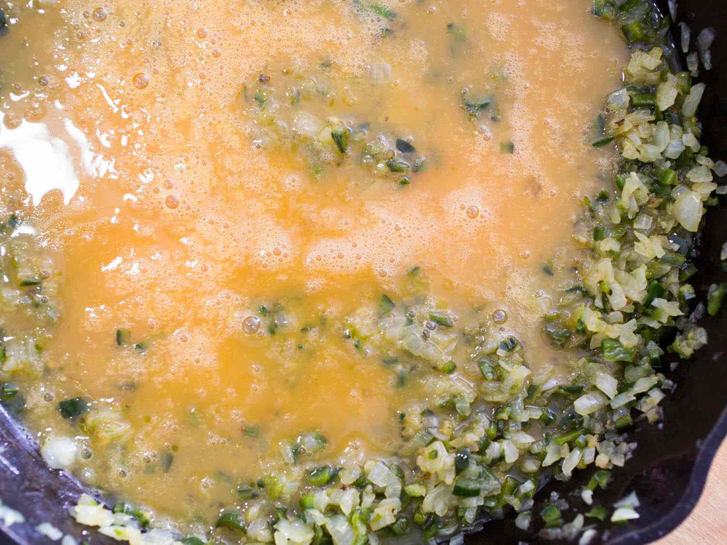 Adding beaten eggs to cooked onions and chile peppers in a skillet.