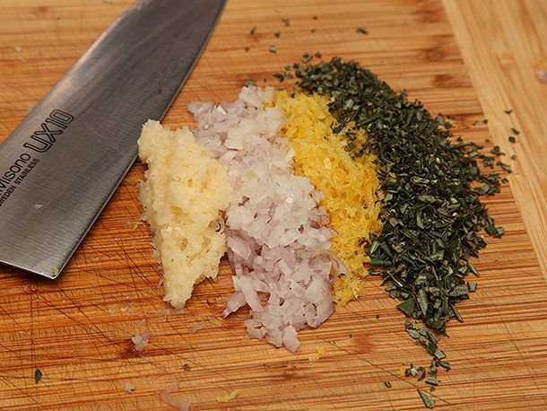 Minced garlic, shallots, lemon zest, and rosemary on a cutting board.