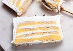 Overhead angle of 2 slices of Lemon Meringue Icebox cake on a marble plate. In the top right corner, there is a spoon with a bite of lemon meringue pie on it 