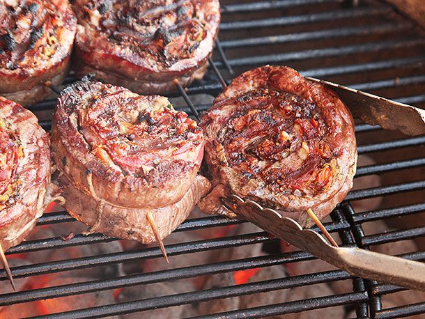 Tongs flipping a stuffed and rolled flank steak on barbecue with coals underneath