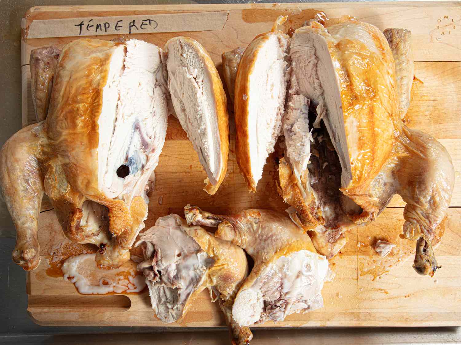 Carved cooked chicken on a wooden cutting board labeled tempered at the top