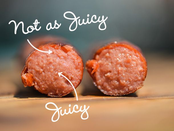 A grilled, natural-casing hot dog that has been cut in half. The cut interior of both halves are facing the camera. Superimposed text reading "Juicy" is linked by an arrow to the center of the hot dog. Text reading "Not as Juicy" is linked by an arrow to the area of the hot dog just under the casing.