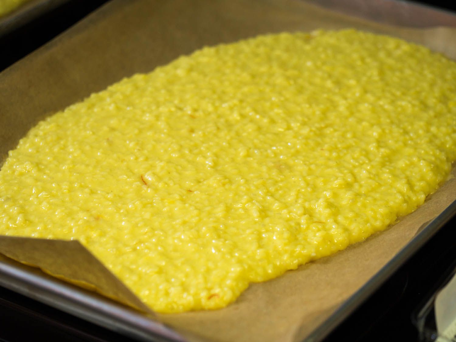 A parchment-lined baking sheet containing a thick layer of the saffron-tinted rice-bechamel mixture.