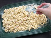 a hand scooping macaroni salad from the le creuset platter