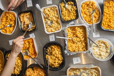 Multiple trays of mac and cheese with utensils part of a foodtasting or comparison event
