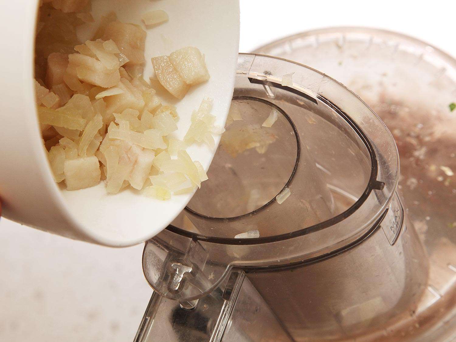Adding chilled fat and onions to the feed chute of a running food processor.