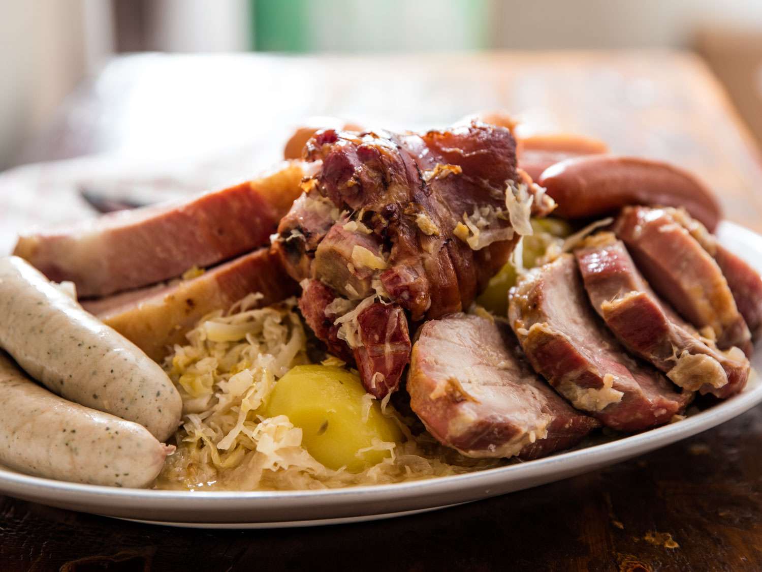 Close-up of choucroute garnie. Sauerkraut and a lone potato occupy a small gap between the various sausages and slices of fresh and cured pork.