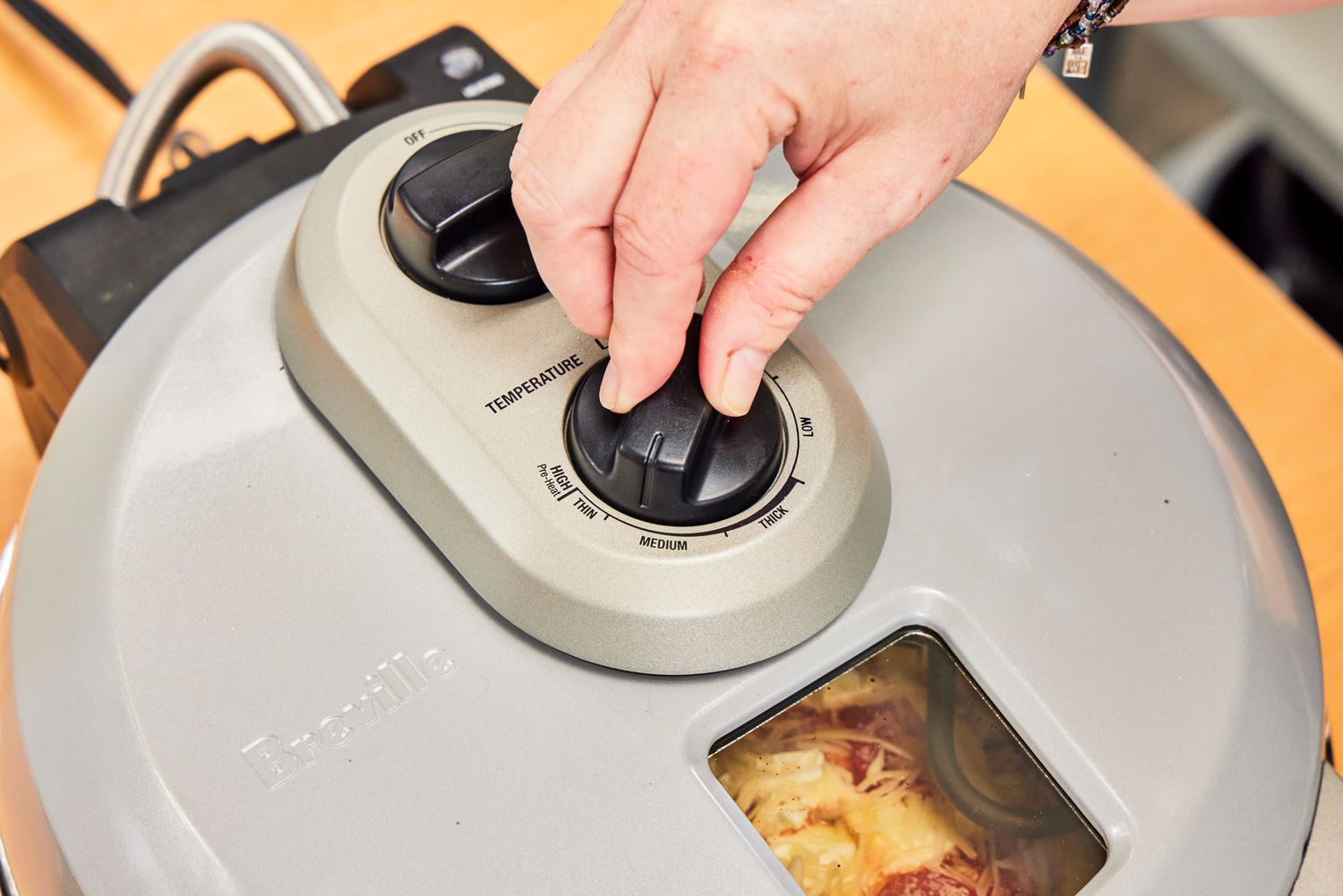 A person adjusting the control dial of the Breville pizza maker.