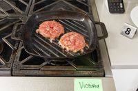 Two burger patties being cooked on the Victoria Cast Iron Square Grill Pan.