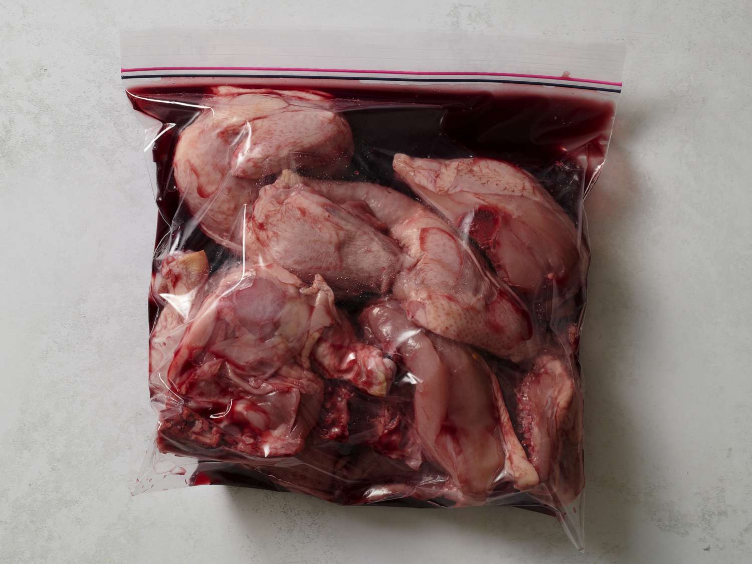 Chicken pieces marinating in red wine inside of a zipper-lock bag.