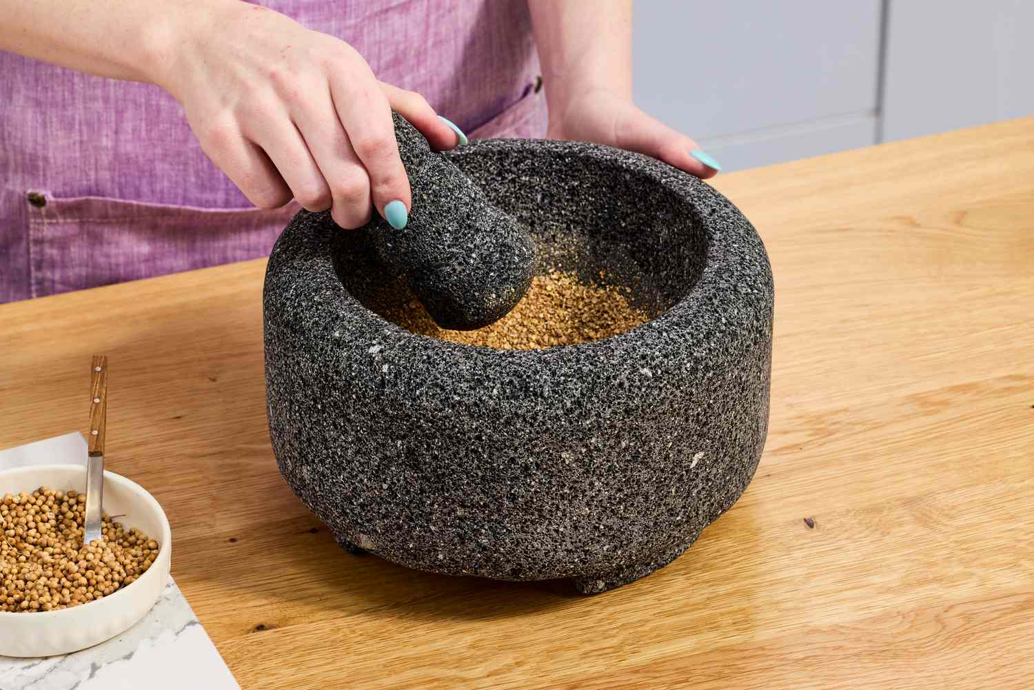 A person using a molcajete to crush coriander seeds.