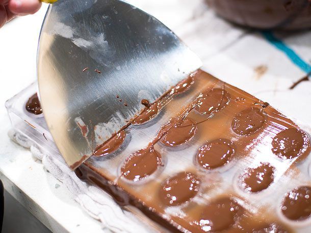 Scraping excess chocolate from bonbon molds.