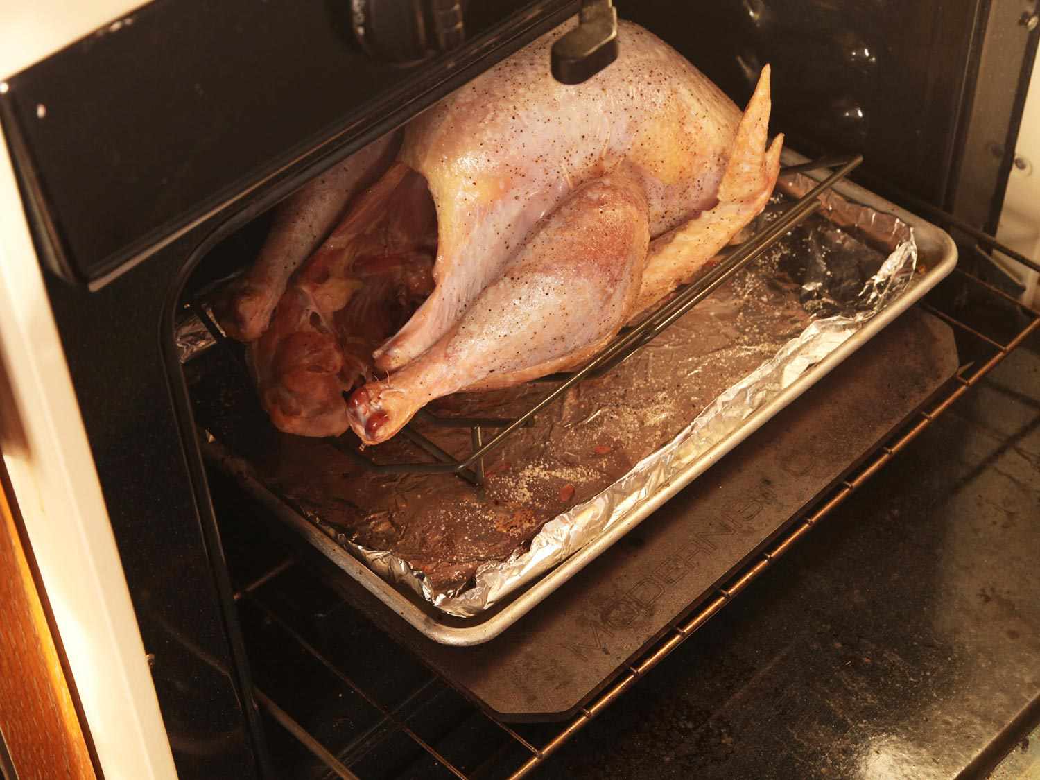 Turkey in a V-rack on a rimmed baking sheet in the oven.