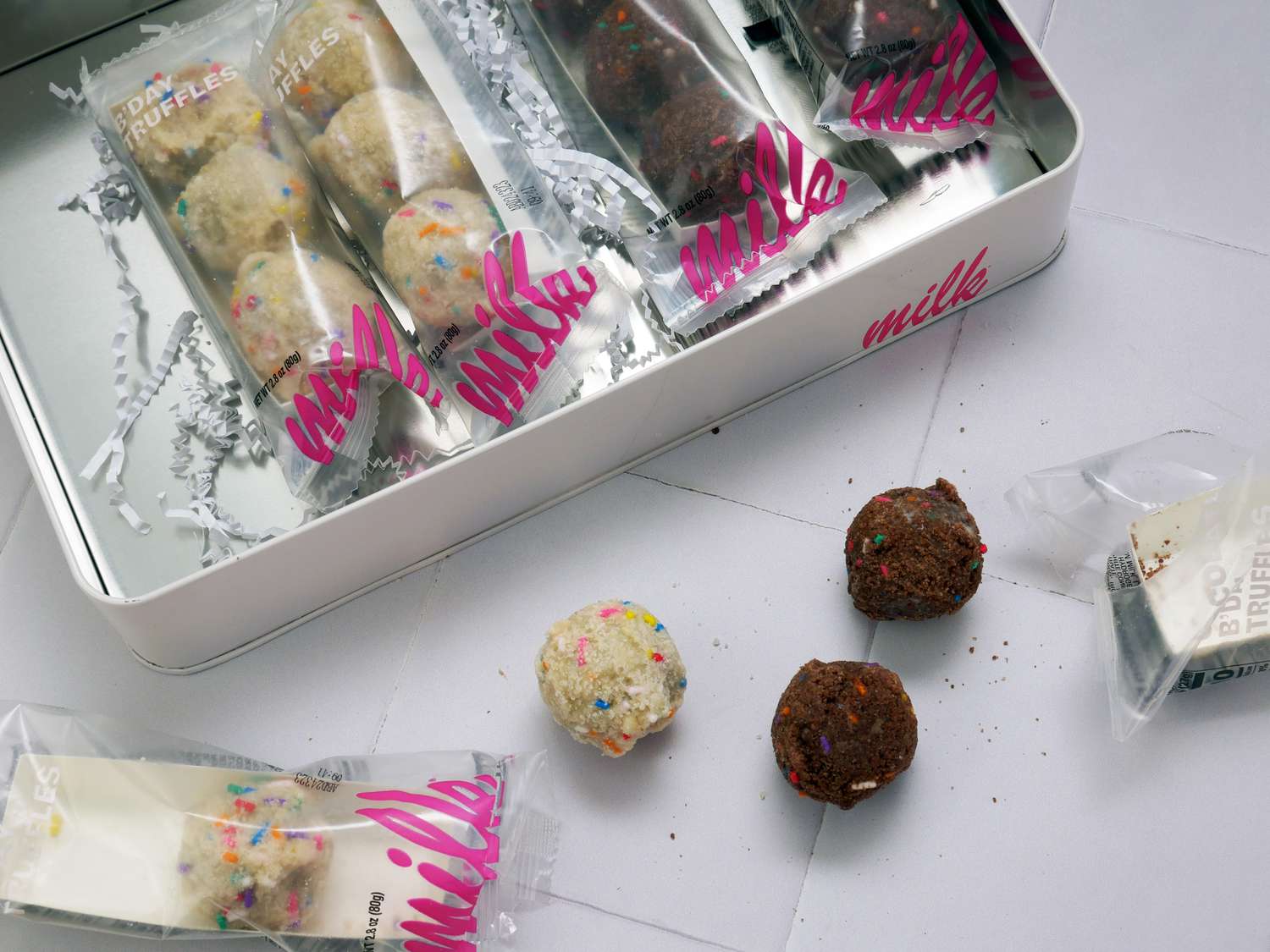 view of box of wrapped truffles and three truffles on white tile surface