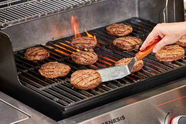 A person flips meat in the Weber Genesis E-335 Gas Grill