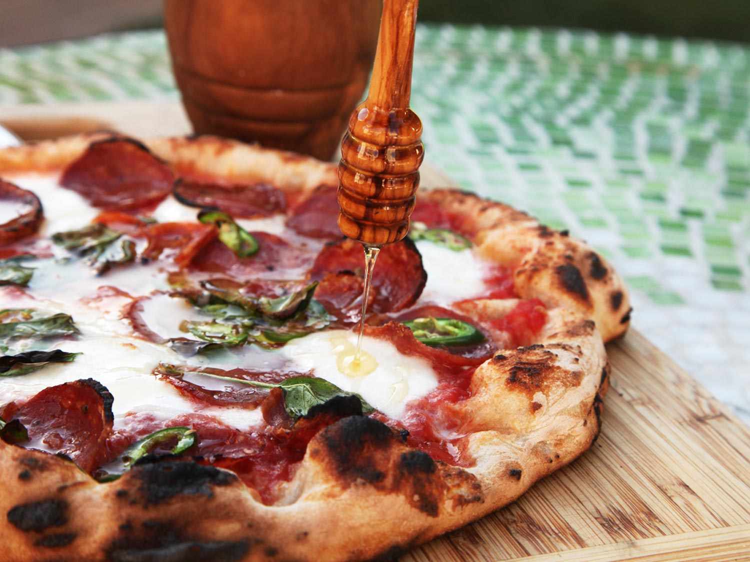 Drizzling honey over baked Neapolitan-style pizza with spicy salami, sliced chiles, and mozzarella