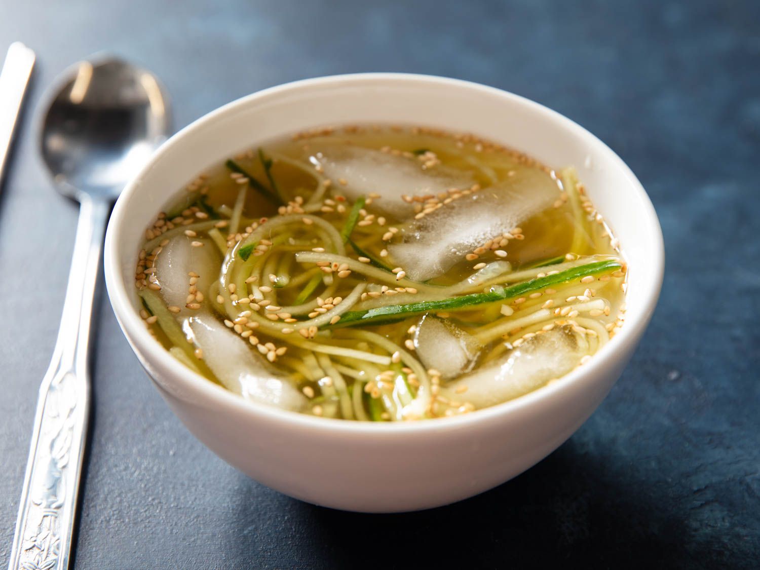 A bowl of cold Korean cucumber soup with ice cubes floating in it.